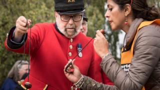 A Chelsea Pensioner wearing his uniform competes with a woman wearing a puffer jacket.