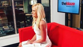 Tomi Lahren sitting on a couch in front of a screen for 'theblaze'