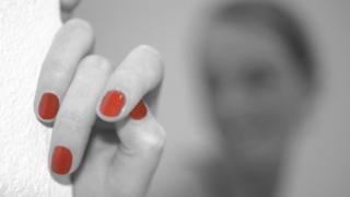 Mano con uñas rojas en primer plano y rostro borroso atrás