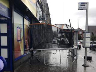 A trampoline stuck between a shop and a bus stop.