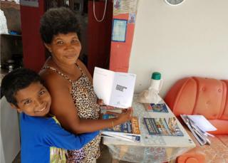 Damiao embraces his mother who is holding a book in their home in