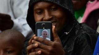 A believer holds a smartphone displaying a picture of Pope Francis as people wait for the arrival of the pope for an open mass at Namugongo Martyrs' Shrine in Namugongo, Uganda, November 28, 2015.