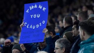 A fan holds up a sign during the English Premier League soccer match between Leicester and Liverpool at The King Power Stadium in Leicester,