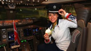Sam Quek in the cockpit of a plane with a pilot's hat on, holding her medal