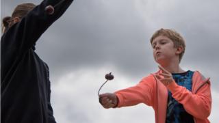 A boy wearing an orange jumper concentrates as he aims his conker.