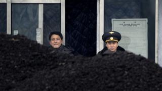 This picture taken on 14 December 2012 from China's northeastern city of Dandong, looking across the border, shows a North Korean military officer (R) and a North Korea man (L) standing behind a pile of coal along the banks of the Yalu River in the northeast of the North Korean border town of Siniuju.