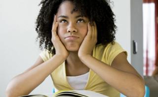 A girl with an afro seated a desk with a book