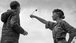 A girl in cadet gear and a boy looking on watch her conker flying in the air.