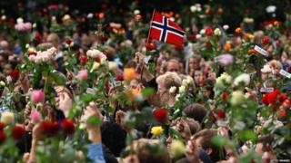 People holding flowers in the air during a flower vigil to remember the victims of the bomb blast and shootings in Norway