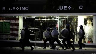 Police in full riot gear run down a shopping street in Peckham, London