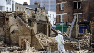 A worker stands by the remains of a furniture shop that was burnt to the ground in Croydon, south London