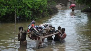 Villagers carry a motorbike on a bed frame through flood water at Golarchi town