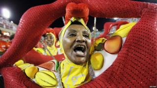 A woman dressed in yellow carrying a huge mouth takes part in the opening night of Rio carnival.