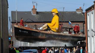 Little Girl Giant rides through the streets of Liverpool on a boat.