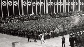 The torchbearer at the 1936 Olympic Games walks through a crowd.