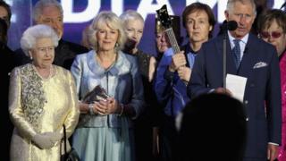 The Queen, Duchess of Cornwall, and Sir Paul McCartney standing next to the Prince of Wales as he gives a speech