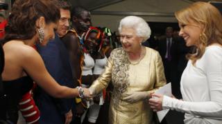 The Queen shaking hands with Cheryl as Kylie watches.