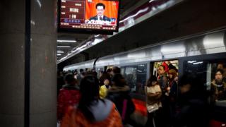 Subway commuters beneath a subway station television showing a live broadcast of Chinese President Hu Jintao's remarks during the opening session of the Communist Party congress in Beijing, 8 November 2012
