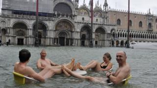 People sit at the table of a bar in a flooded St. Mark's Square in Venice, Italy, Sunday, Nov. 11, 2012.