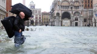 A man carries luggage on a flooded St Mark's square during a "acqua alta" on November 11, 2012 in Venice.