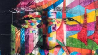 A close up of the mural shows a man's face merged with abstract shapes and bright colours.