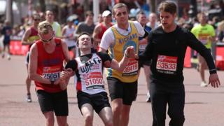 Three runners help another cross the finish line