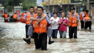 A policeman carries a man on his back as he walks on a flooded street after heavy rainfalls hit Chengdu, Sichuan province, 9 July 2013