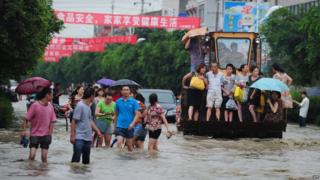 Residents travel on an excavator as others commute through flooded streets in a district in Chengdu, southwest China's Sichuan province.