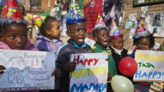Children in party hats with colourful balloons celebrating Nelson Mandela's birthday.