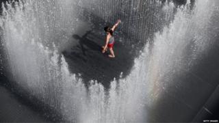 A girl enjoying the hot weather, surrounded by water fountains