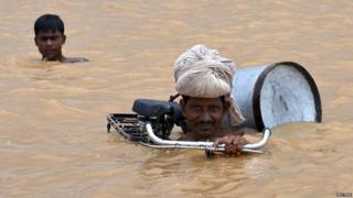 A flood-affected man with his bicycle moves to a safer place. He is submerged to his shoulders in water.