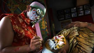 Performers in Taiwan prepare by painting their faces like fierce bright masks for Guanjiang Shou.
