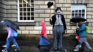 A performer stands in the rain as people pass by.