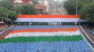 Children sitting in rows beneath a flag
