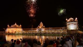 Golden temple lit up at night with fireworks bursting above it
