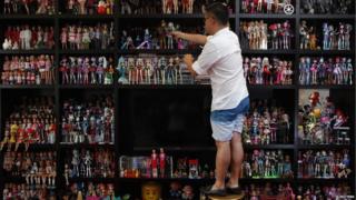 Man places a doll with his collection of thousands on a shelf.