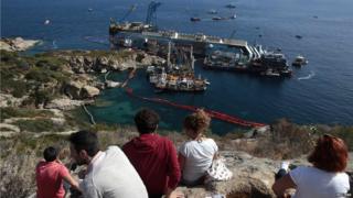 A group of onlookers sit on nearby land and watch the salvage attempt of the Costa Concordia.