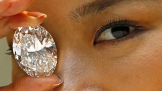A model holds up a white diamond larger than her eye.