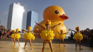 Girls dress as ducks as people gather to see a giant Rubber Duck by Dutch conceptual artist Florentijin Hofman at Glory Pier on September 19, 2013 in Kaohsiung, Taiwan.