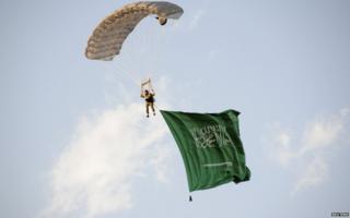 A parachutist descends from the sky carrying the national flag of Saudi Arabia