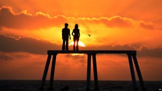 The sun rises over the giant sculpture of a man and woman situated 300 yards out to sea off the coast of Northumberland at Newbiggin-by-the-Sea. Comprising of two 5 metre tall bronze figures of a man and a woman the sculpture is called "the couple" and is by artist Sean Henry.