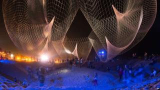 Visitors explore the creation of artist Janet Echelman "The Space Between Us" during Glow 2013 on September 29, 2013 at the beach in Santa Monica, California. Glow is an all-night cultural experience featuring original commissions by artists that re-imagine Santa Monica Beach as a playground for thoughtful and participatory temporary artworks.