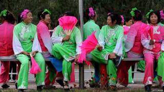 A group of Chinese women dressed in traditional costumes rest on a bench as they wait to perform for the cyclists during the third stage of the 2013 Tour of Beijing