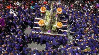 Group of people dressed in purple robes carry a painting