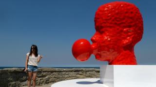 A tourist poses beside a two-metre-high blood red sculpture of a head blowing bubble gum by Qian Sihua, which is part of the Sculpture by the Sea exhibition which runs on the Bondi to Tamarama coastal walk in Sydney.
