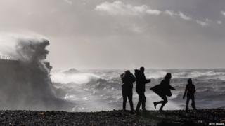 Braving the weather, members of the public in Dover watch large waves produced by the storm break against the harbour wall.