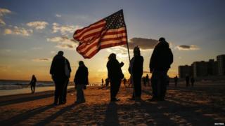 People stand with an American flag on the beach while remembering the storm last year