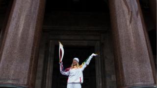 Torchbearer for winter Olympics posing in front of Cathedral in St Petersburg.
