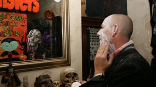 Ian dressed in a scary outfit putting face paint on in front of a mirror