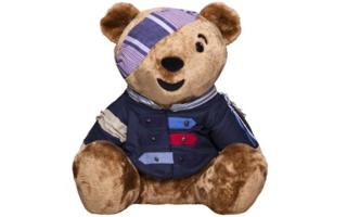 Bear with a blue shirt with patches and buttons and a purple striped bandana.